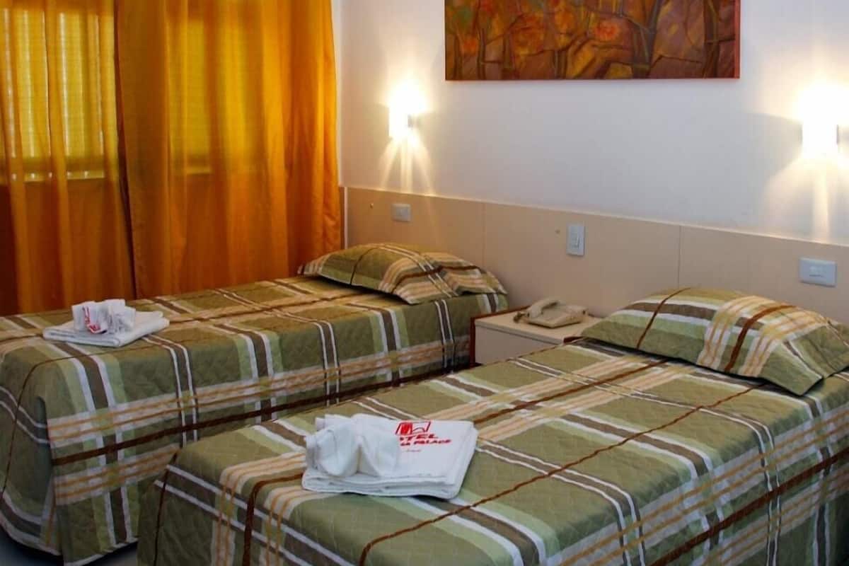 Ein Hotelzimmer mit zwei Einzelbetten, jeweils mit gestreifter Bettdecke und Kissen, einem Nachttisch mit Telefon und einem Bild an der Wand.