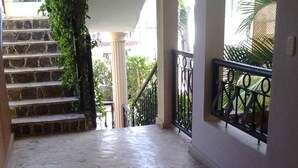 A concrete-floored corridor with a staircase on the left, a metal railing on the right, and a view of the outdoors through a window. - Aparta-Hotel Villa Baya (San Rafael del Yuma)