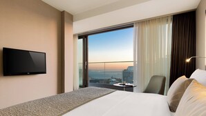 A hotel room with a large bed, a flat-screen TV, a small table with a cup, and a view of the city through a large window. - AC Hotel Istanbul Macka (Istanbul)