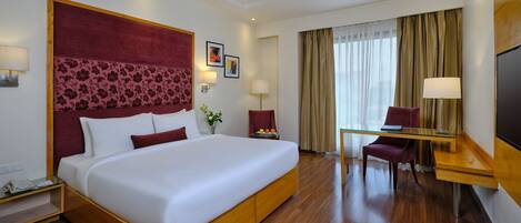 A hotel room with a large bed, a desk with a chair, a television, and a window with curtains.