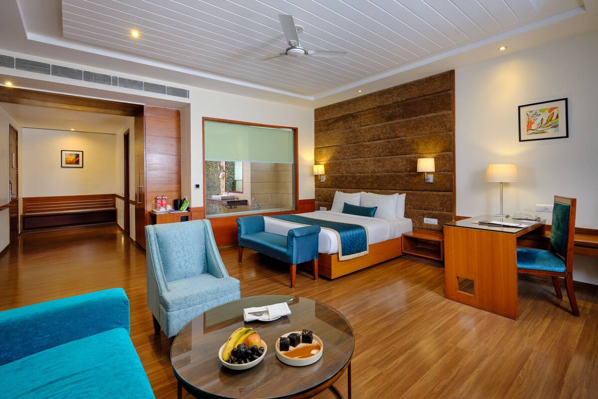 A hotel room with a bed, a desk, a chair, a sofa, and a table with fruit.