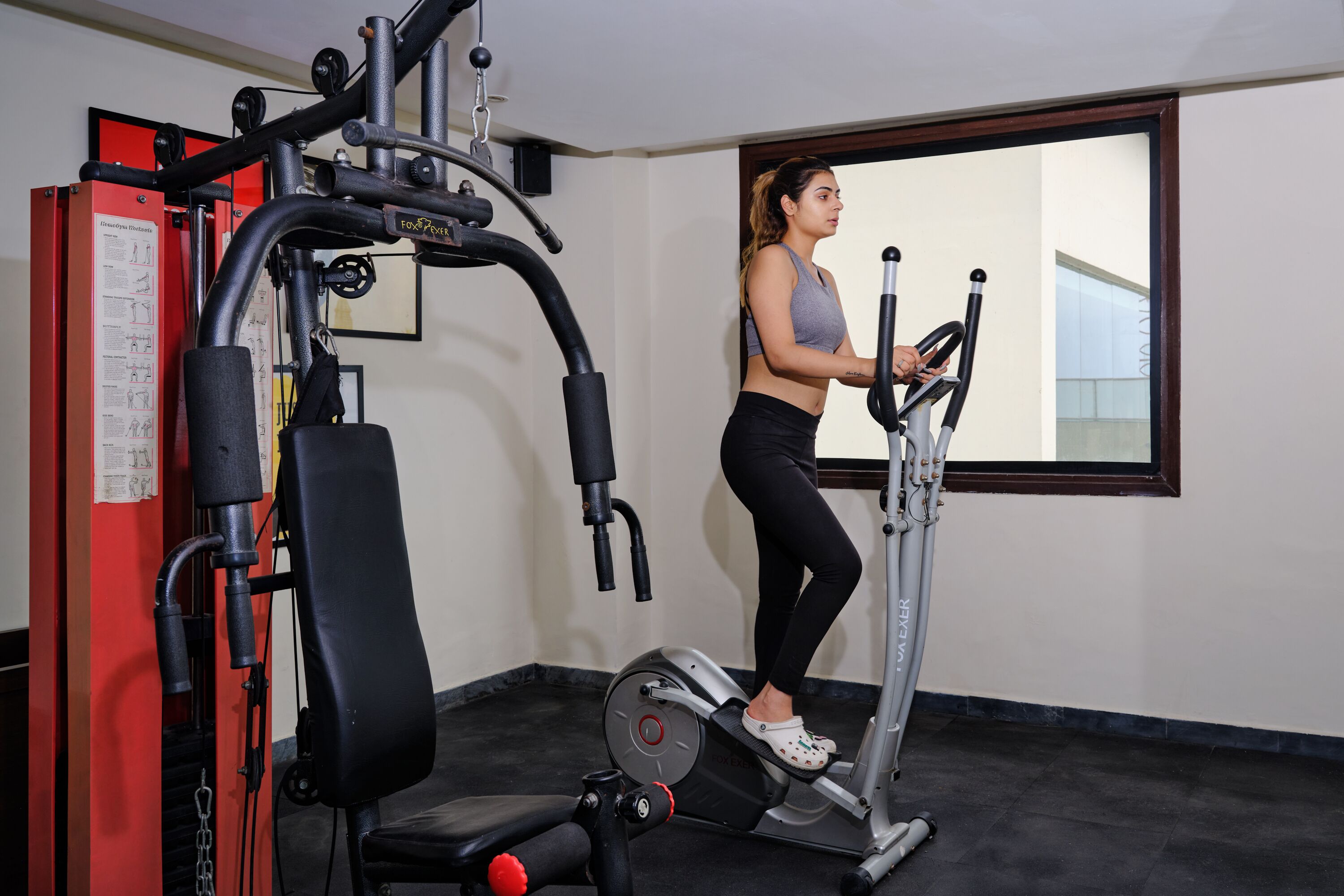 A gym with exercise equipment, a large window, and a red machine.