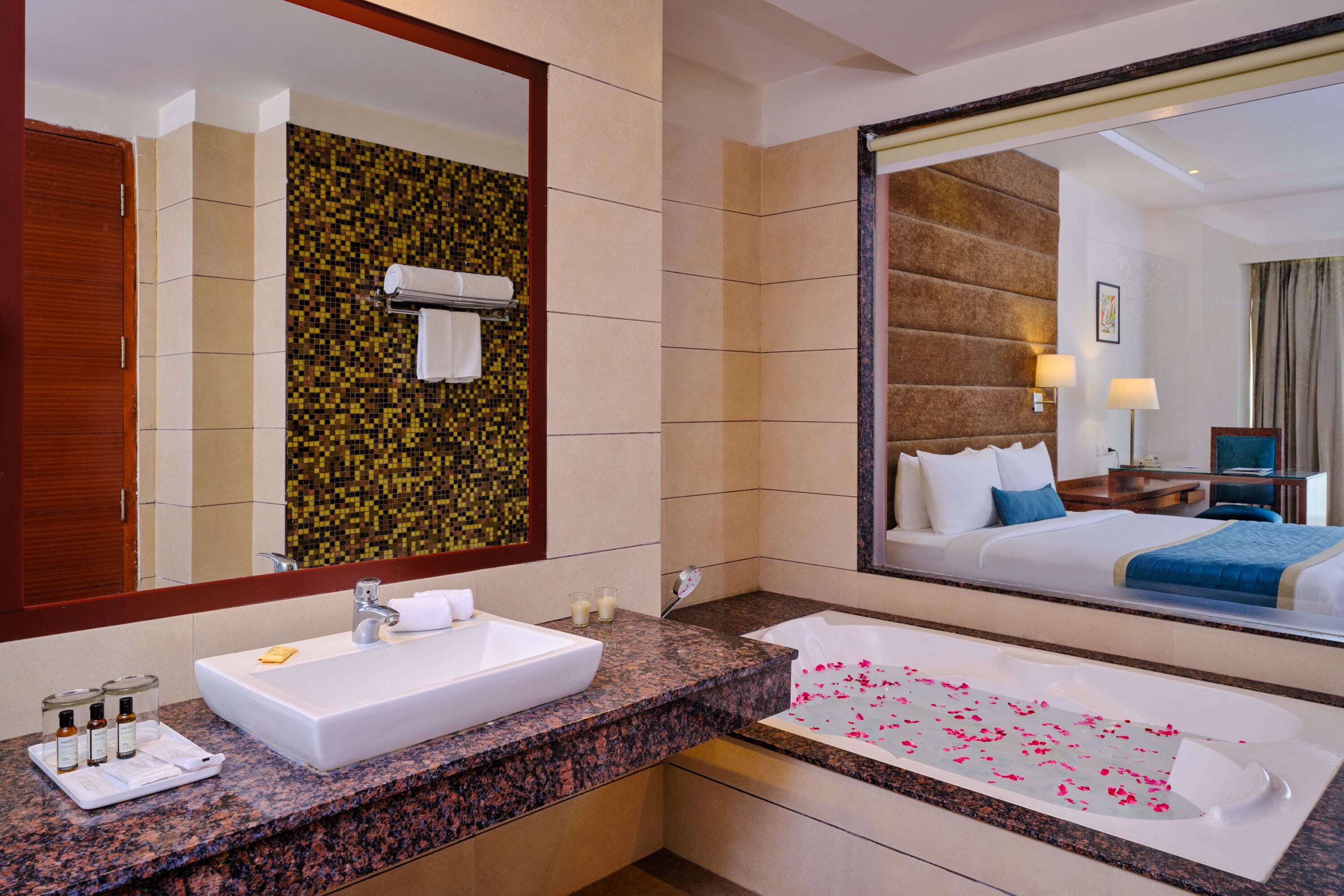 Un baño de hotel con un espejo grande, un lavamanos y una bañera con pétalos de rosa.