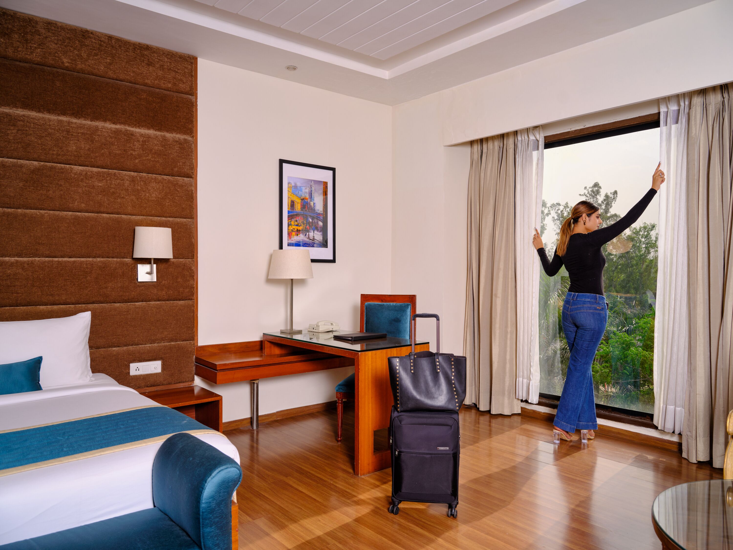 Quarto de hotel com cama, escrivaninha, cadeira e vista para o verde pela janela.