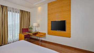 Habitación de hotel con una cama grande, un escritorio con silla, un televisor de pantalla plana montado en la pared y una ventana con cortinas.