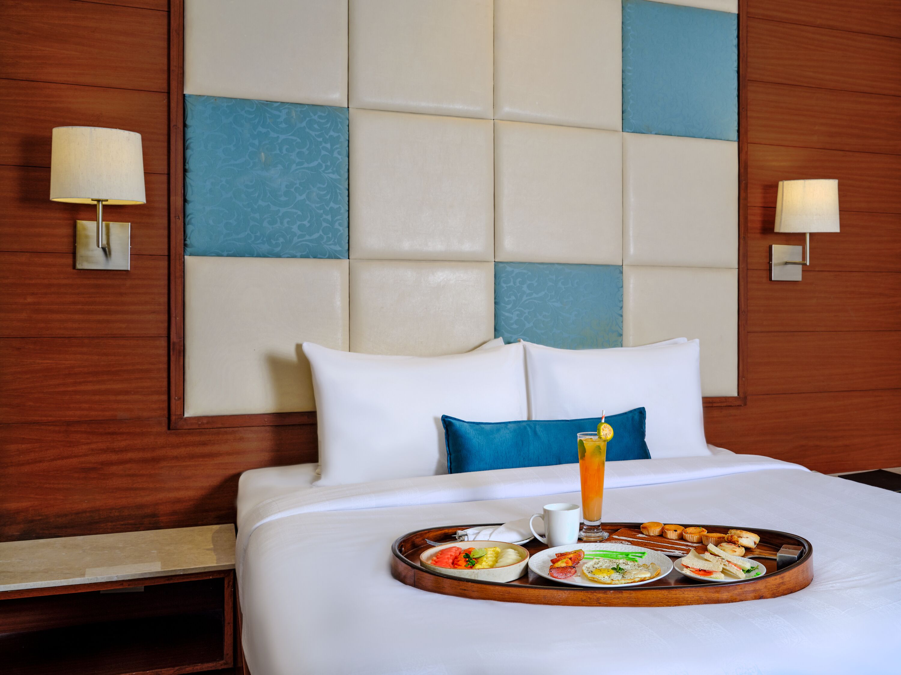 Une chambre d’hôtel avec un lit parfaitement fait, un plateau de petit-déjeuner et un grand panneau mural orné d’un motif bleu et blanc.