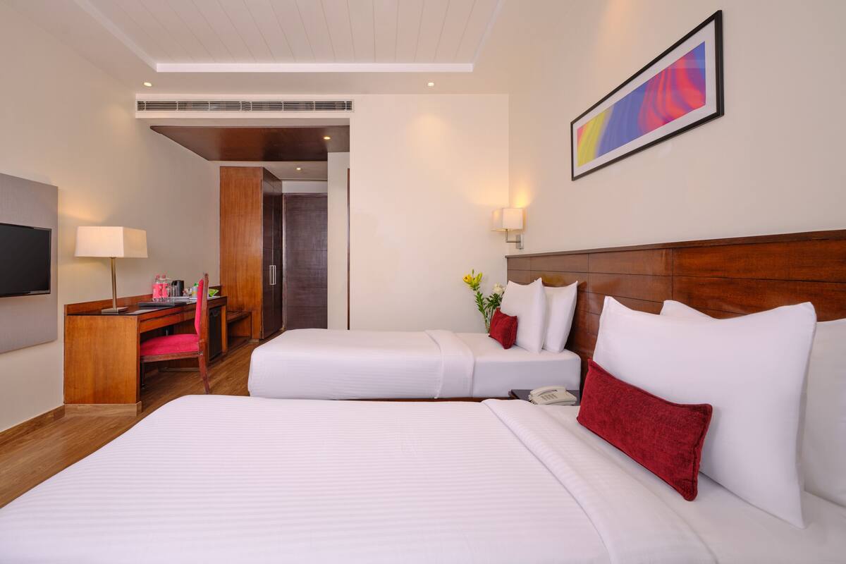 A hotel room with two beds, a desk, a TV, and a painting on the wall.