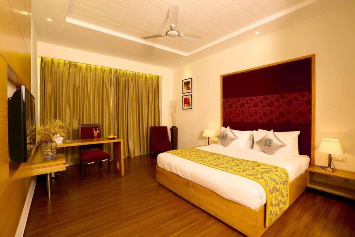 A hotel room with a large bed, a desk with a chair, a television, and a ceiling fan.