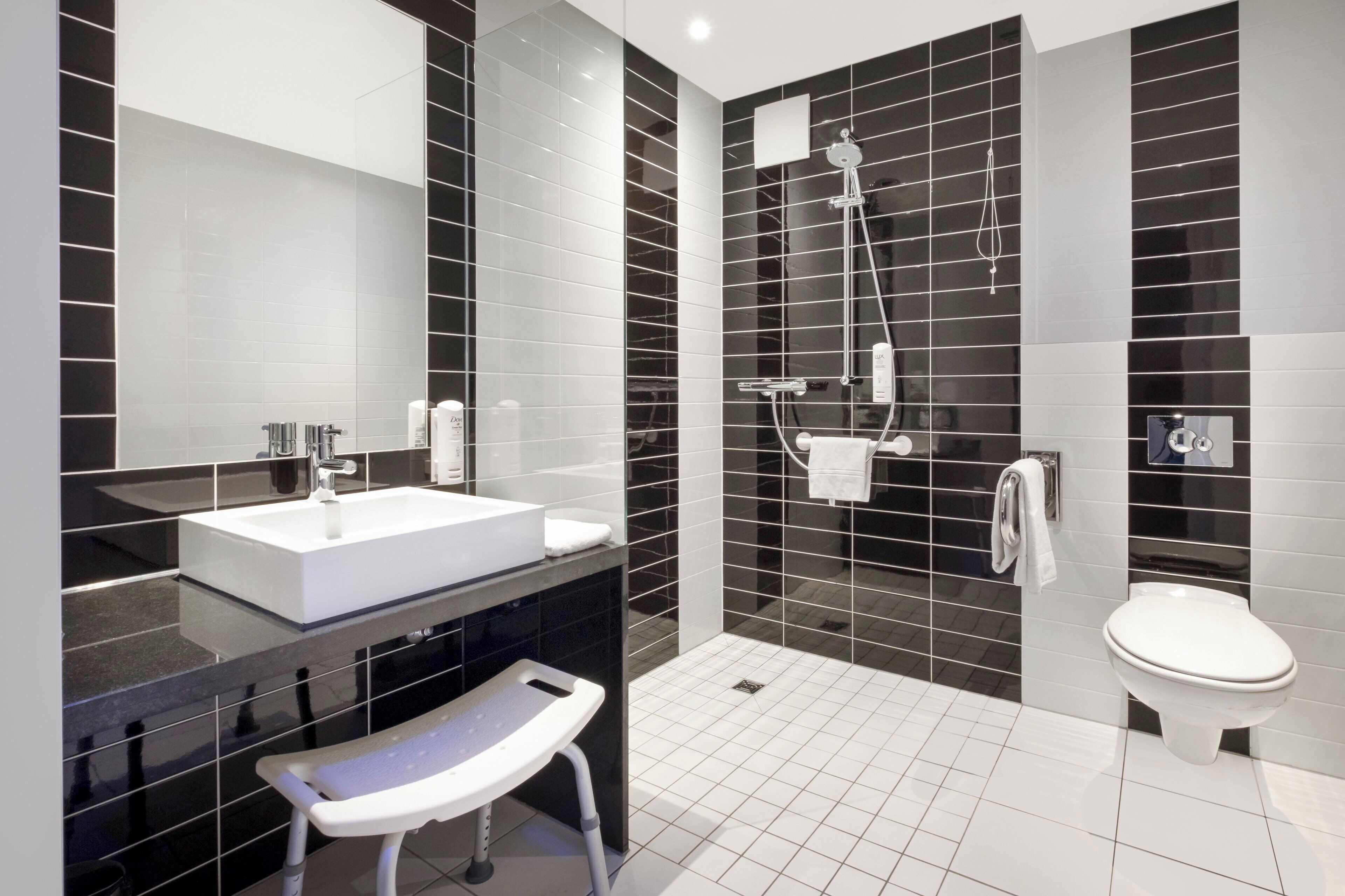 A modern bathroom with a white sink, black and white tiled walls, a shower, and a toilet.