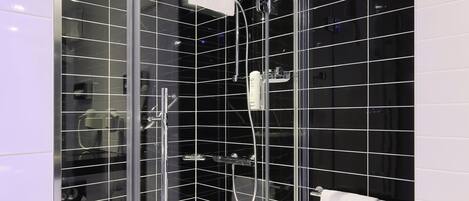Un baño moderno con ducha acristalada, paredes de azulejos negros y un inodoro blanco.