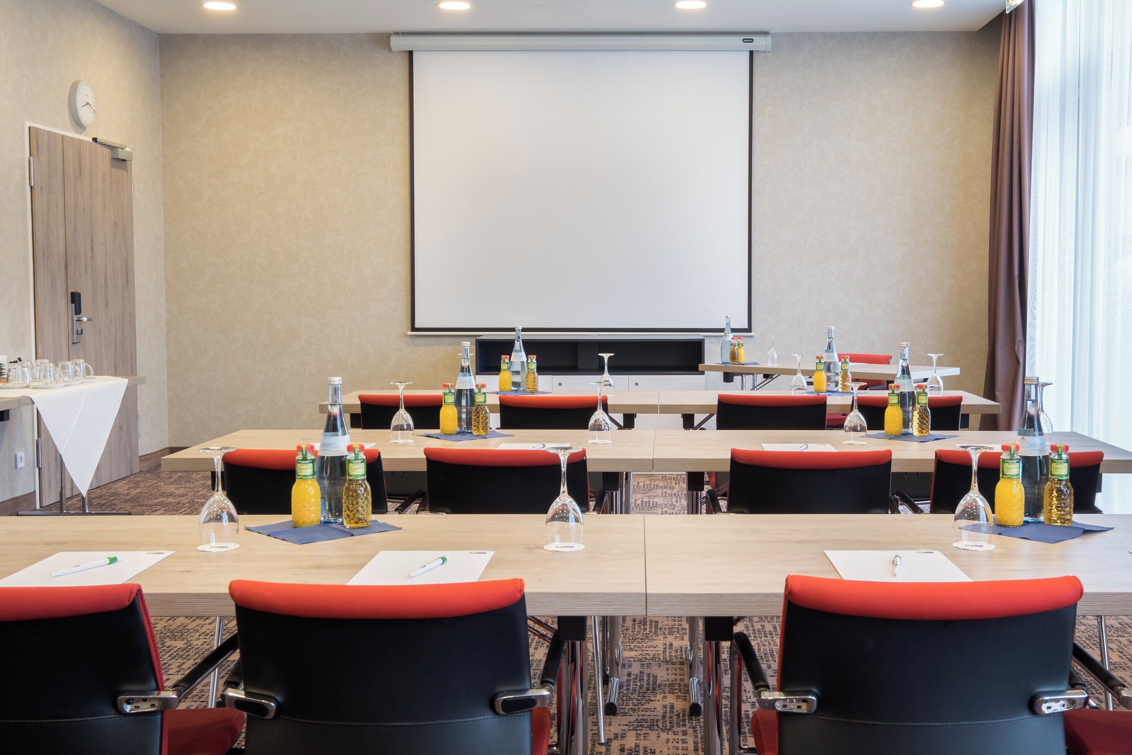 Ein Konferenzraum mit Projektionsleinwand, Tischen mit Stühlen sowie verschiedenen Flaschen und Gläsern.