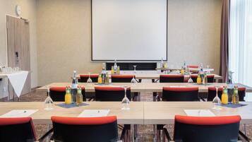 Ein Konferenzraum mit Projektionsleinwand, Tischen mit Stühlen sowie verschiedenen Flaschen und Gläsern.