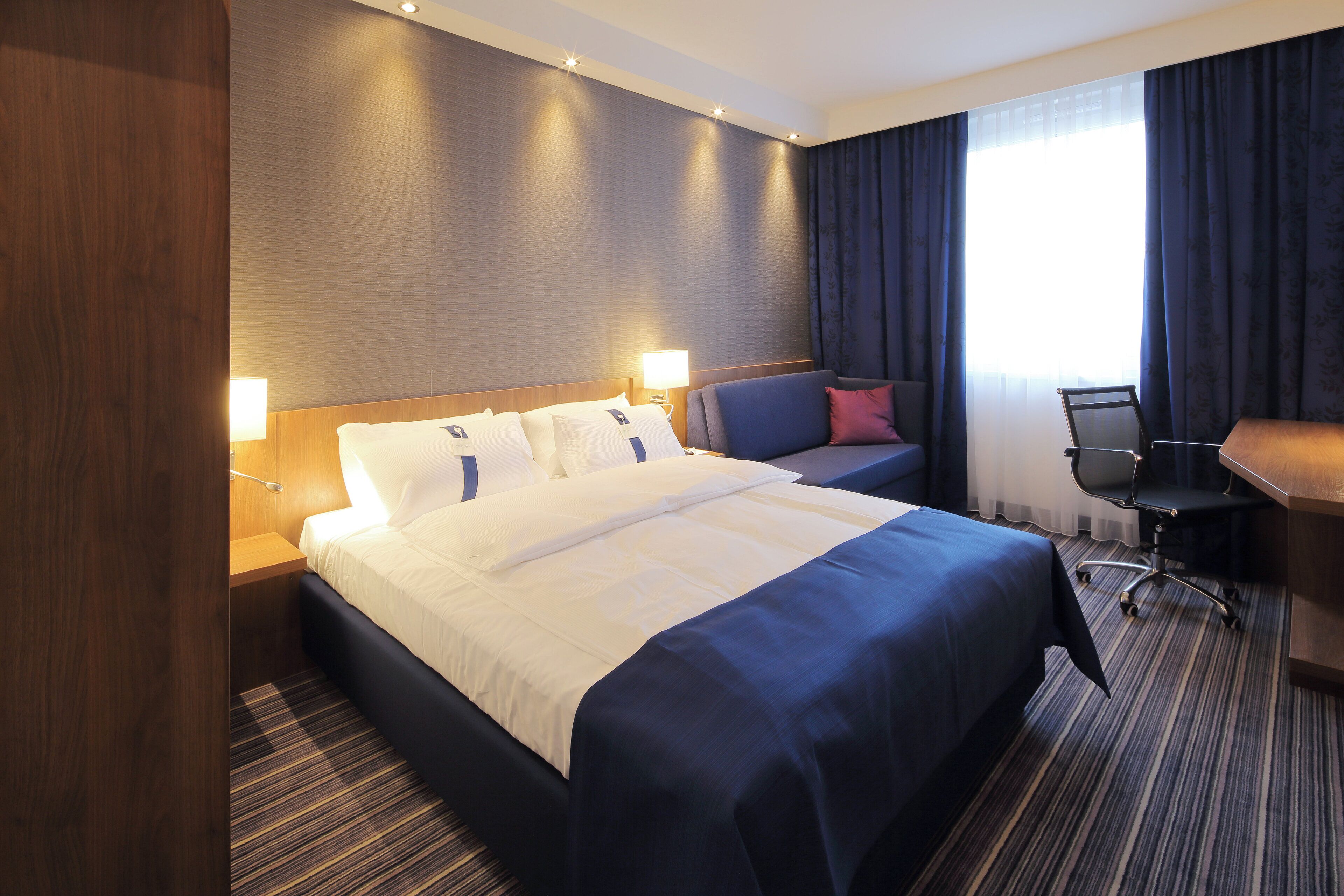 A hotel room with a large bed, bedside lamps, a desk, and a chair.