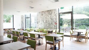 A spacious indoor dining area with multiple tables and chairs, large windows, and a view of greenery outside. - Holiday Inn Express Friedrichshafen by IHG (Friedrichshafen)