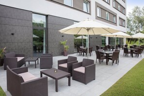 An outdoor seating area with wicker furniture and umbrellas, a modern building in the background, and a well-maintained lawn. - Holiday Inn Express Friedrichshafen by IHG (Friedrichshafen)