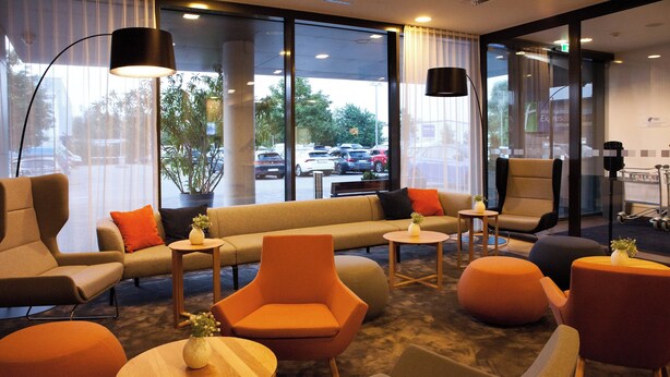 A modern hotel lobby with a sofa, chairs, and tables. - Holiday Inn Express Friedrichshafen by IHG (Friedrichshafen)
