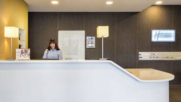 A hotel reception desk with a receptionist, a digital display, and a Holiday Inn Express sign.