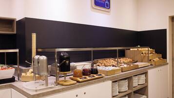 Un buffet proposant divers plats, une machine à café et un panneau indiquant un panier de fruits à la disposition des clients.
