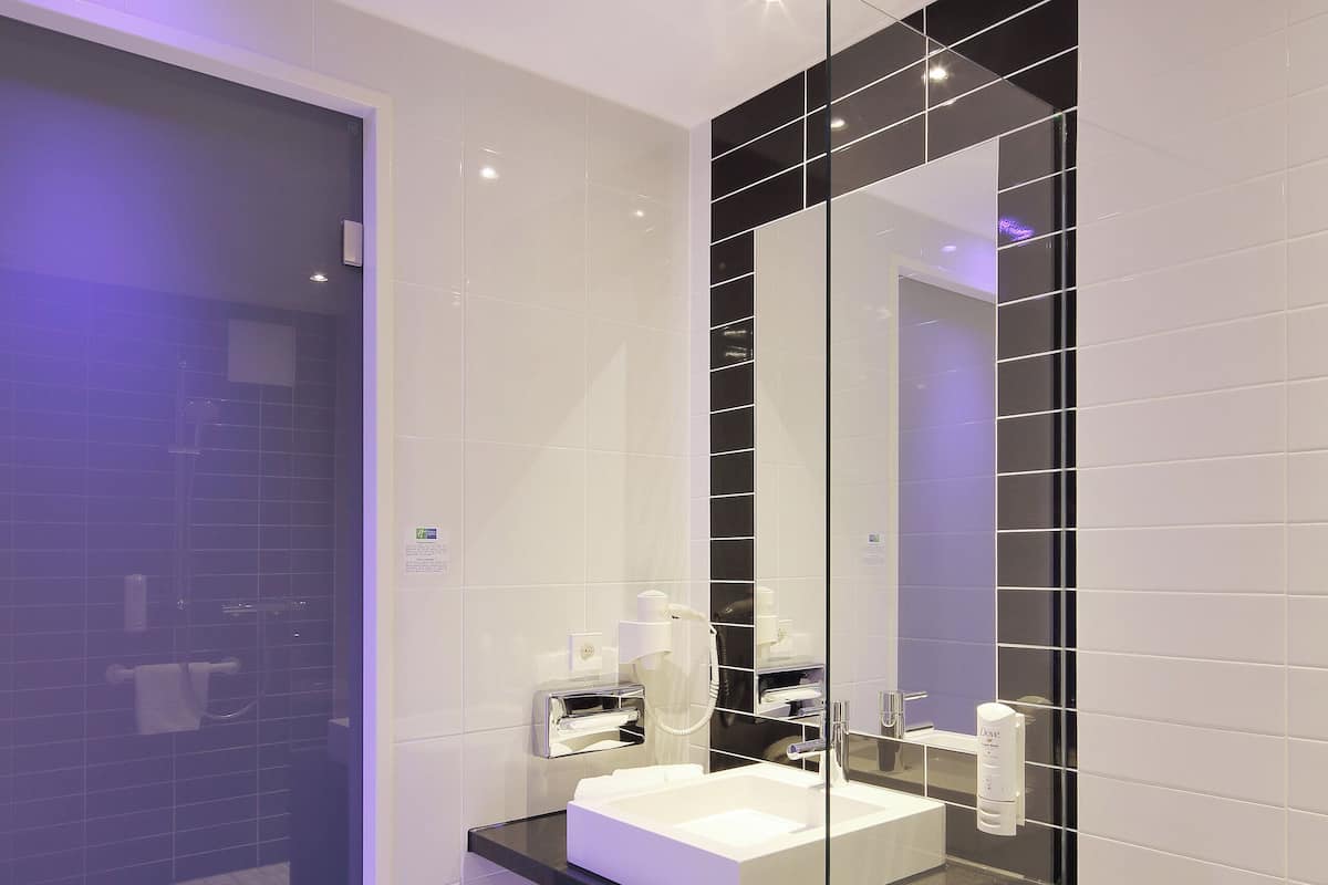 A modern bathroom with a large mirror, white sink, and black-tiled walls.