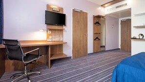 A hotel room with a wooden desk, a black office chair, a flat-screen TV mounted on the wall, and a wardrobe with a mirror. - Holiday Inn Express Friedrichshafen by IHG (Friedrichshafen)