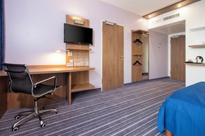 A hotel room with a wooden desk, a black office chair, a flat-screen TV mounted on the wall, and a wardrobe with a mirror. - Holiday Inn Express Friedrichshafen by IHG (Friedrichshafen)