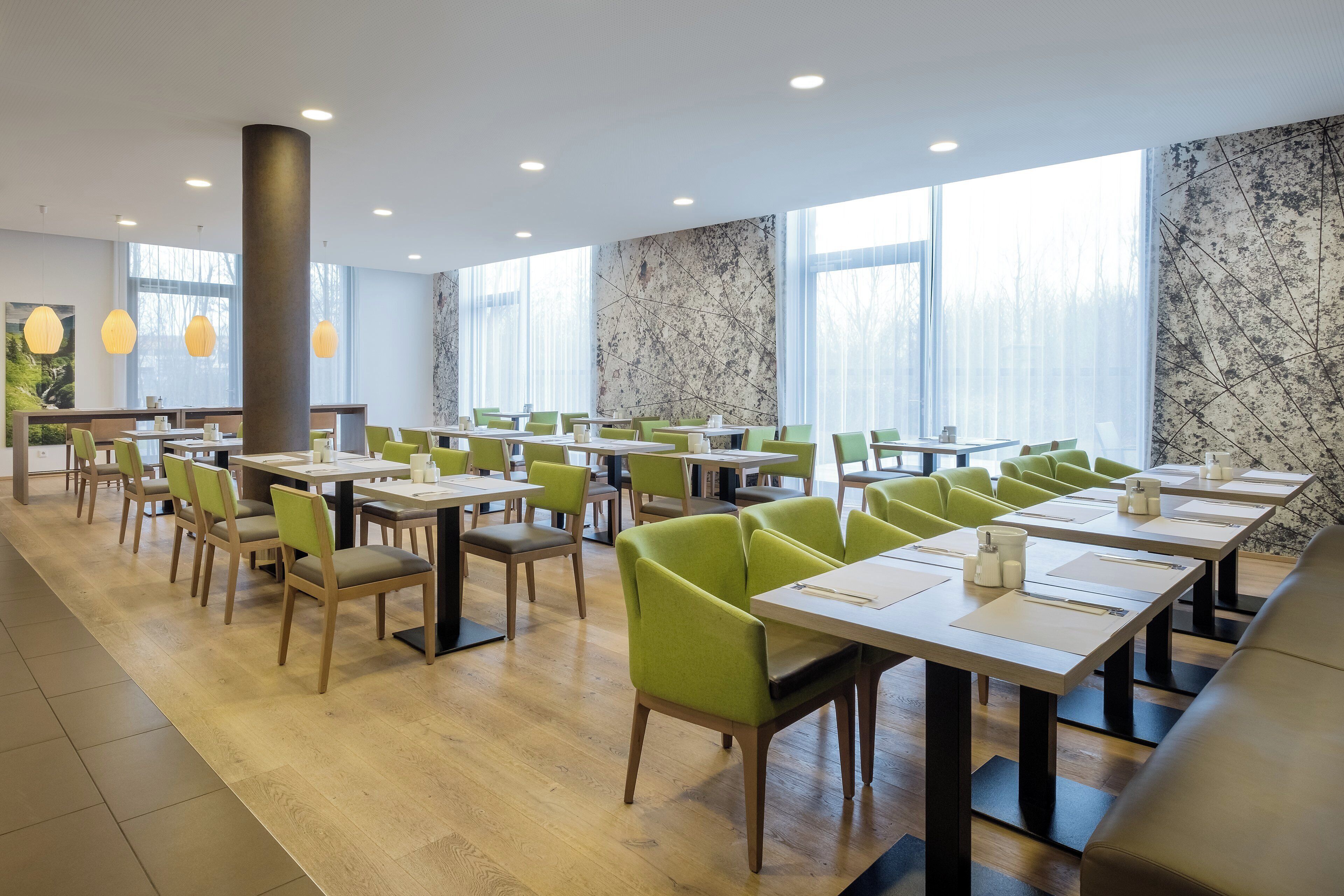 A modern dining area with multiple tables and chairs, large windows, and a marble wall.