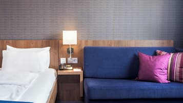A hotel room with a bed, a blue sofa, a nightstand with a lamp, and a wall with a textured pattern.