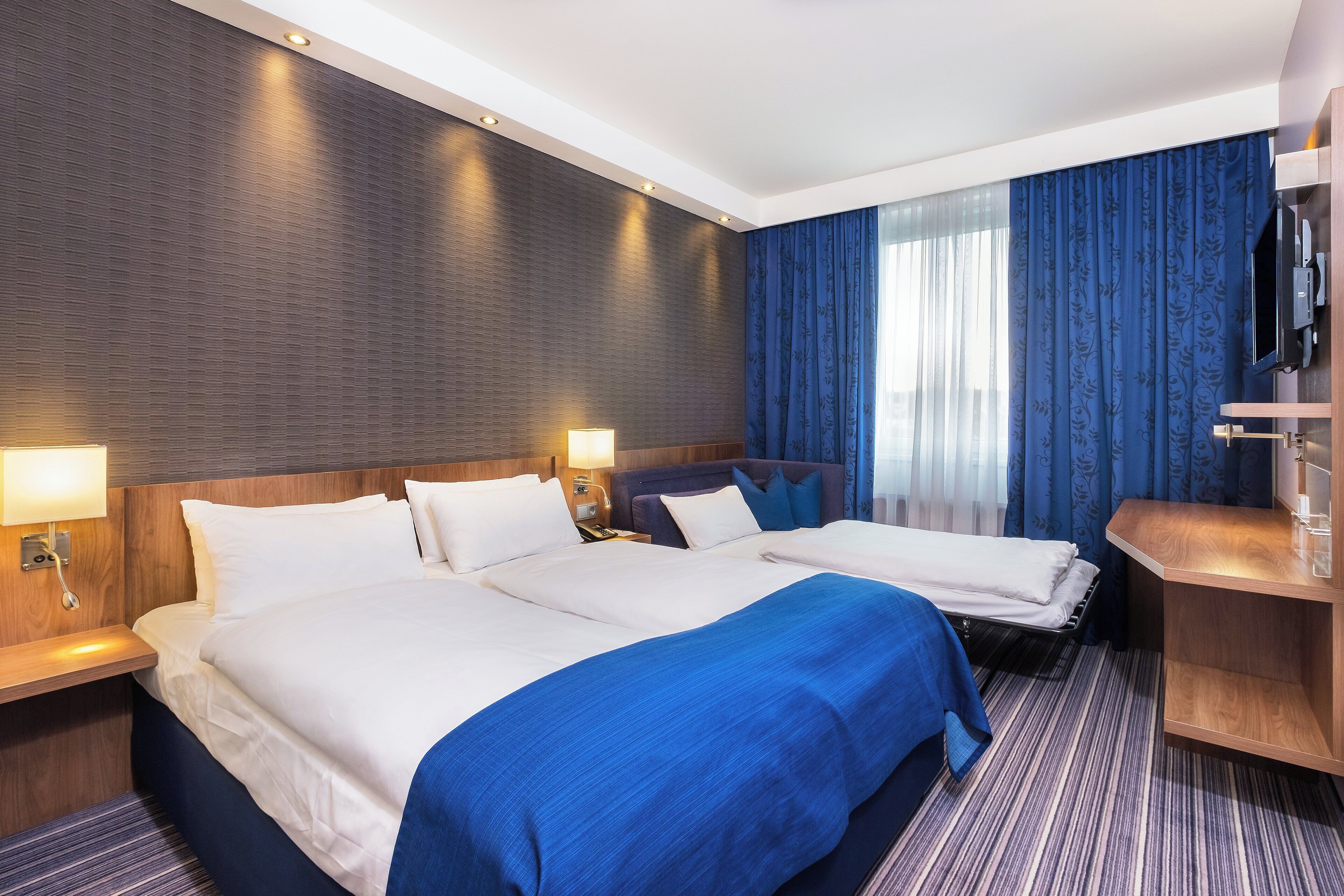 A hotel room with two beds, a desk, a TV, and a bathroom.