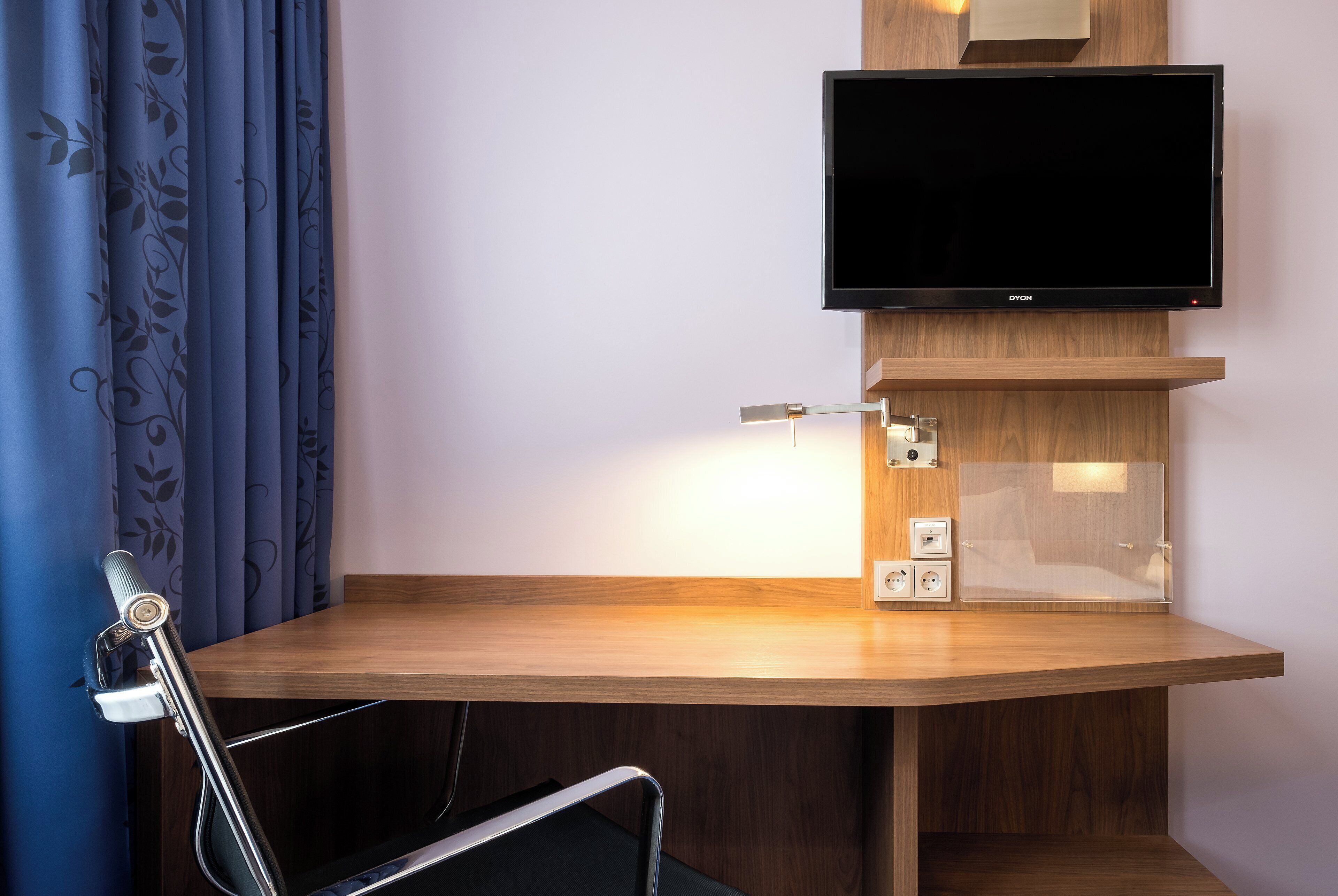 Une chambre d’hôtel avec un bureau en bois, un téléviseur à écran plat fixé au mur, une lampe de bureau et une chaise.