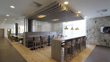 A modern restaurant interior with wooden flooring, a central bar area, and seating arrangements.