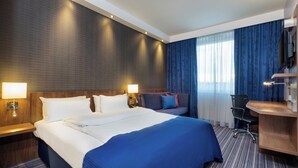 A hotel room with a large bed, two bedside lamps, a desk with a chair, a TV, and a window with curtains. - Holiday Inn Express Friedrichshafen by IHG (Friedrichshafen)