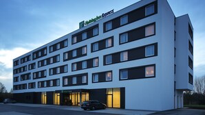 A modern hotel building with a flat facade, multiple windows, and a visible entrance with a car parked outside. - Holiday Inn Express Friedrichshafen by IHG (Friedrichshafen)