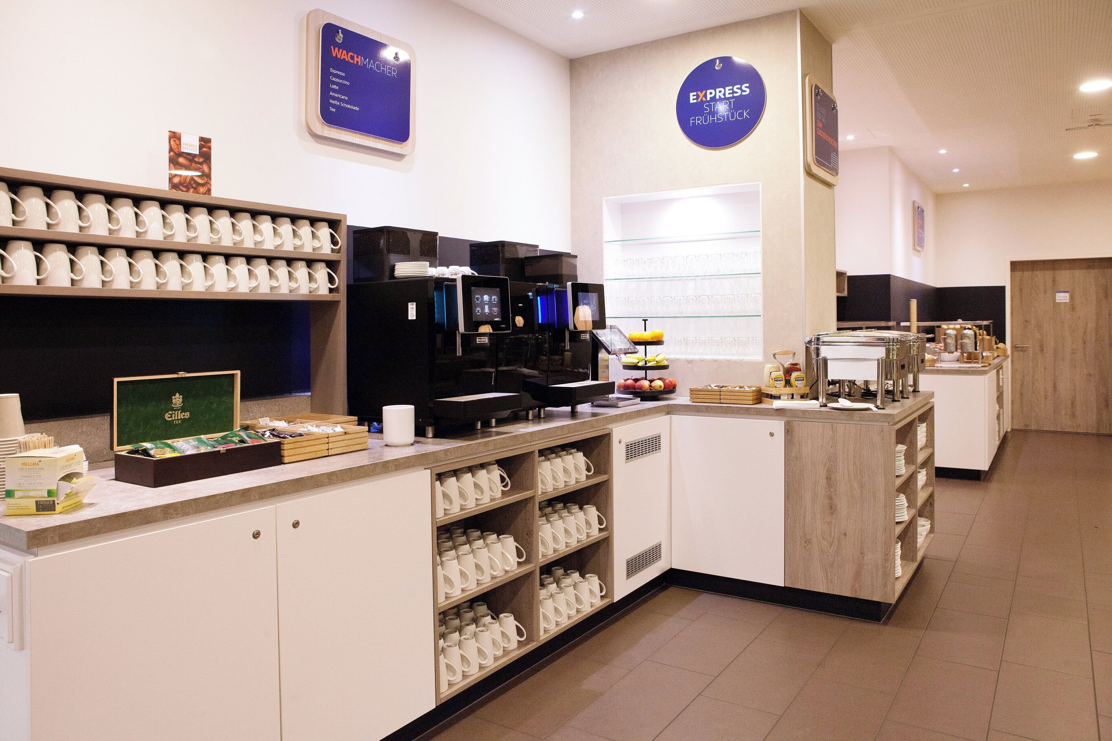 Um espaço com estação de café, várias máquinas de café, exposição de xícaras e diversas opções de comida.