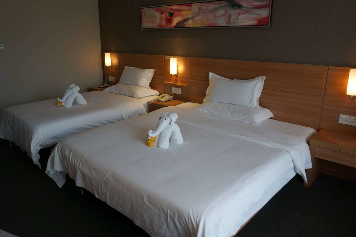 Une chambre d’hôtel avec deux lits, chacun équipé de draps blancs et d’une serviette blanche. Des lampes murales sont fixées de chaque côté des lits.