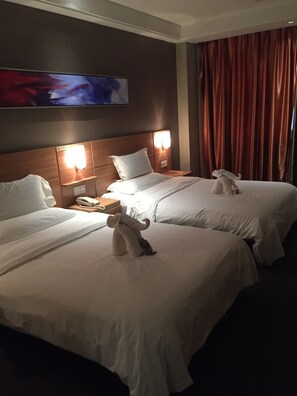 Une chambre d’hôtel avec deux lits, chacun doté de draps et d’oreillers blancs, d’une tête de lit en bois, de lampes de chevet, d’un téléphone et d’un tableau au mur.