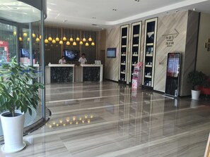 Un espace d’accueil d’hôtel au design moderne, comprenant un comptoir d’accueil, un écran numérique et un répertoire des services proposés.