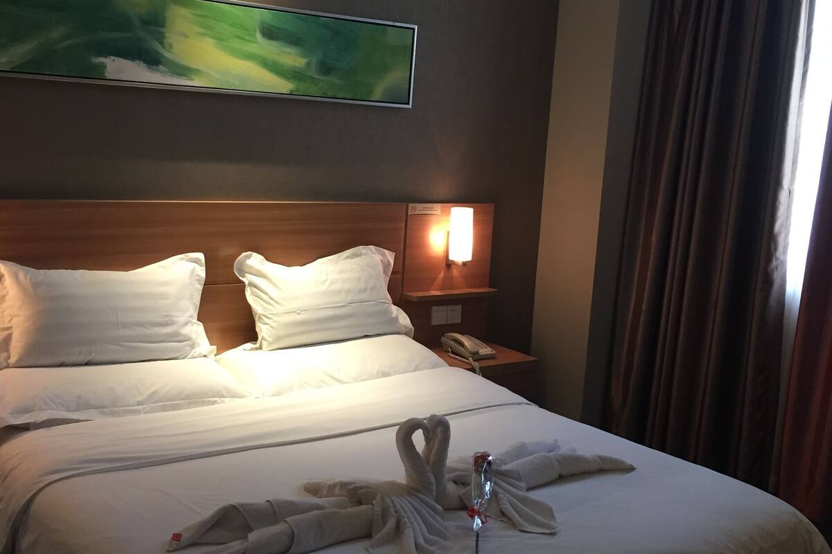 Une chambre d’hôtel avec un lit bien fait, un téléviseur à écran plat fixé au mur, une lampe de chevet et un téléphone sur une table de chevet.