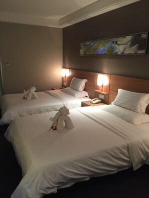 Une chambre d’hôtel avec deux lits, chacun doté de draps et d’oreillers blancs, d’une tête de lit en bois, de lampes de chevet et d’un tableau au mur.