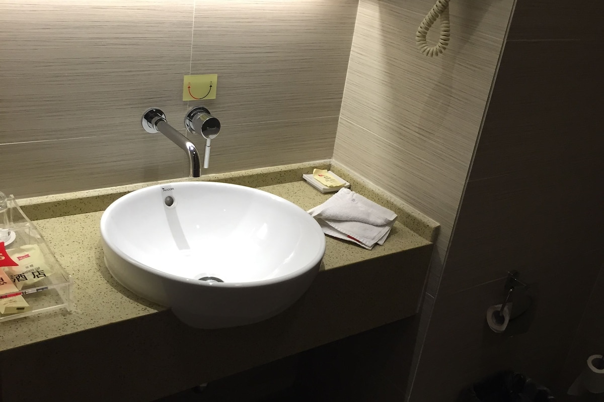 Een badkamer met een wit wastafelmeubel, een spiegel, een haardroger en een prullenbak.