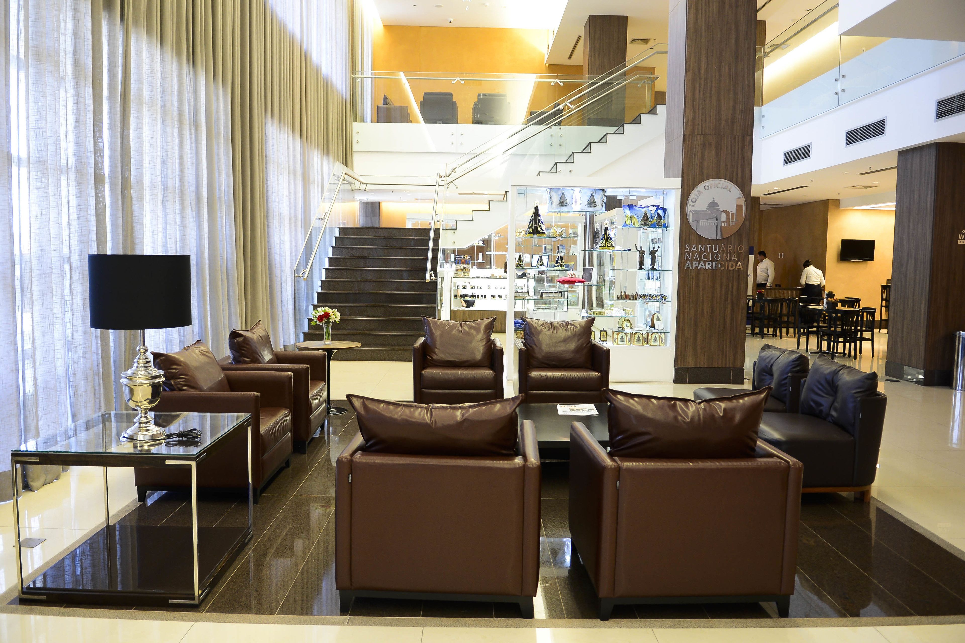 A modern lobby with leather sofas, a glass coffee table, and a staircase leading to an upper level.