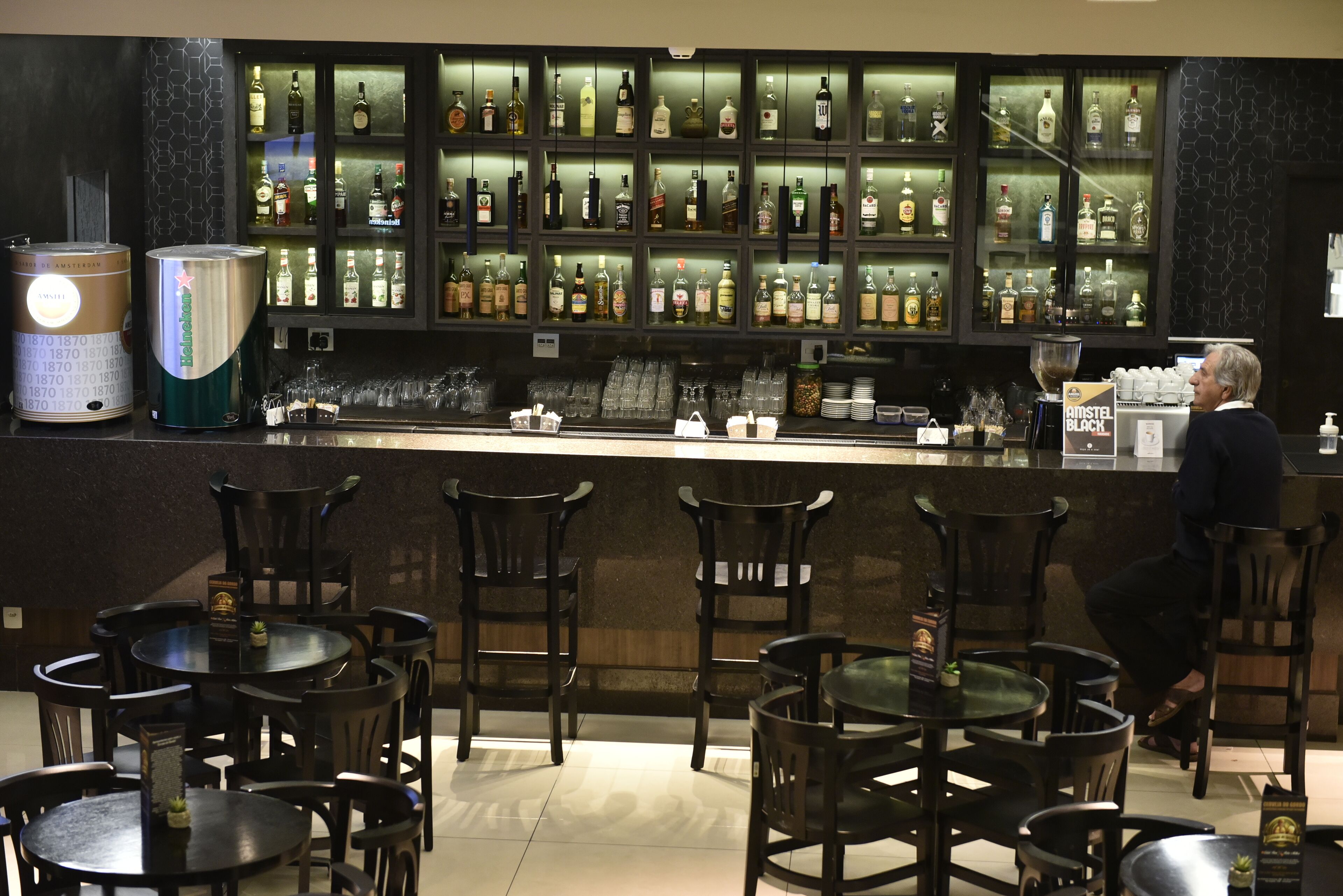 A bar area with a variety of liquor bottles on shelves, a coffee machine, and several tables and chairs.