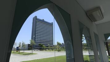 A view through a glass archway of a modern building with a parking lot and greenery in the foreground.