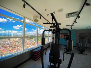 A gym with exercise equipment, large windows with a city view, and a ceiling with recessed lighting. - Hotel Rainha do Brasil (Aparecida)
