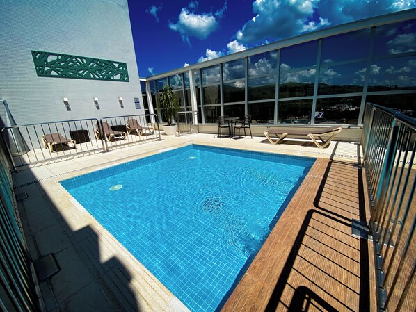A swimming pool with lounge chairs and a view of the cityscape. - Hotel Rainha do Brasil (Aparecida)