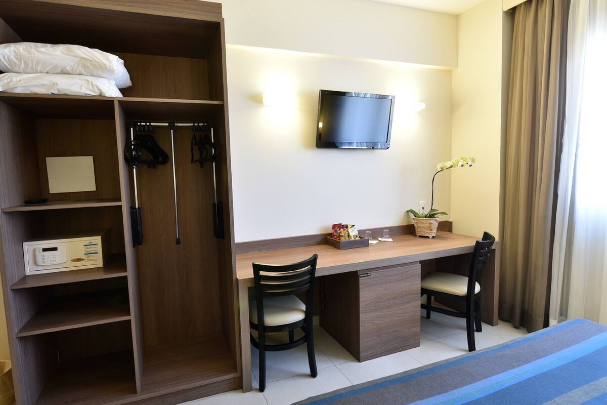 Een hotelkamer met een houten bureau, twee stoelen, een televisie, een kledingkast en een kleine potplant.