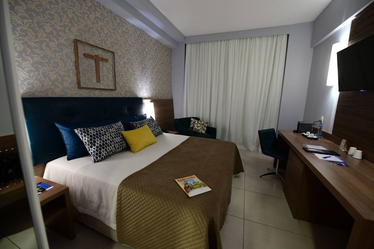 Een hotelkamer met een groot bed, een bureau, een stoel, een televisie en een ingelijst schilderij aan de muur.