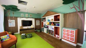 Uma sala de jogos infantil com televisão, estantes de brinquedos e um tapete verde.