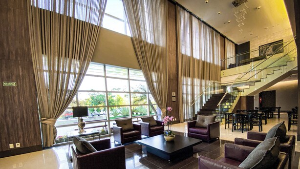 A spacious lobby with a high ceiling, large windows, and a staircase leading to an upper level. - Hotel Rainha do Brasil (Aparecida)