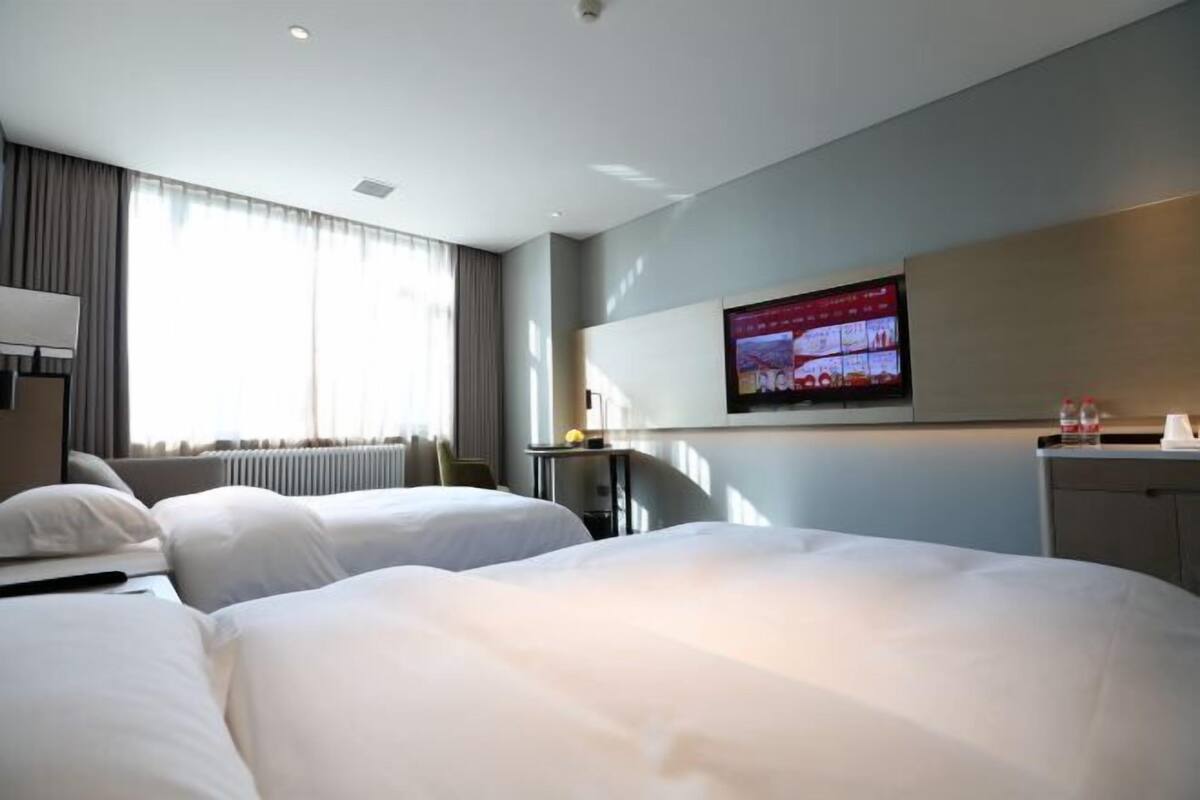 Habitación de hotel con dos camas, un televisor montado en la pared, un escritorio y una ventana con cortinas.