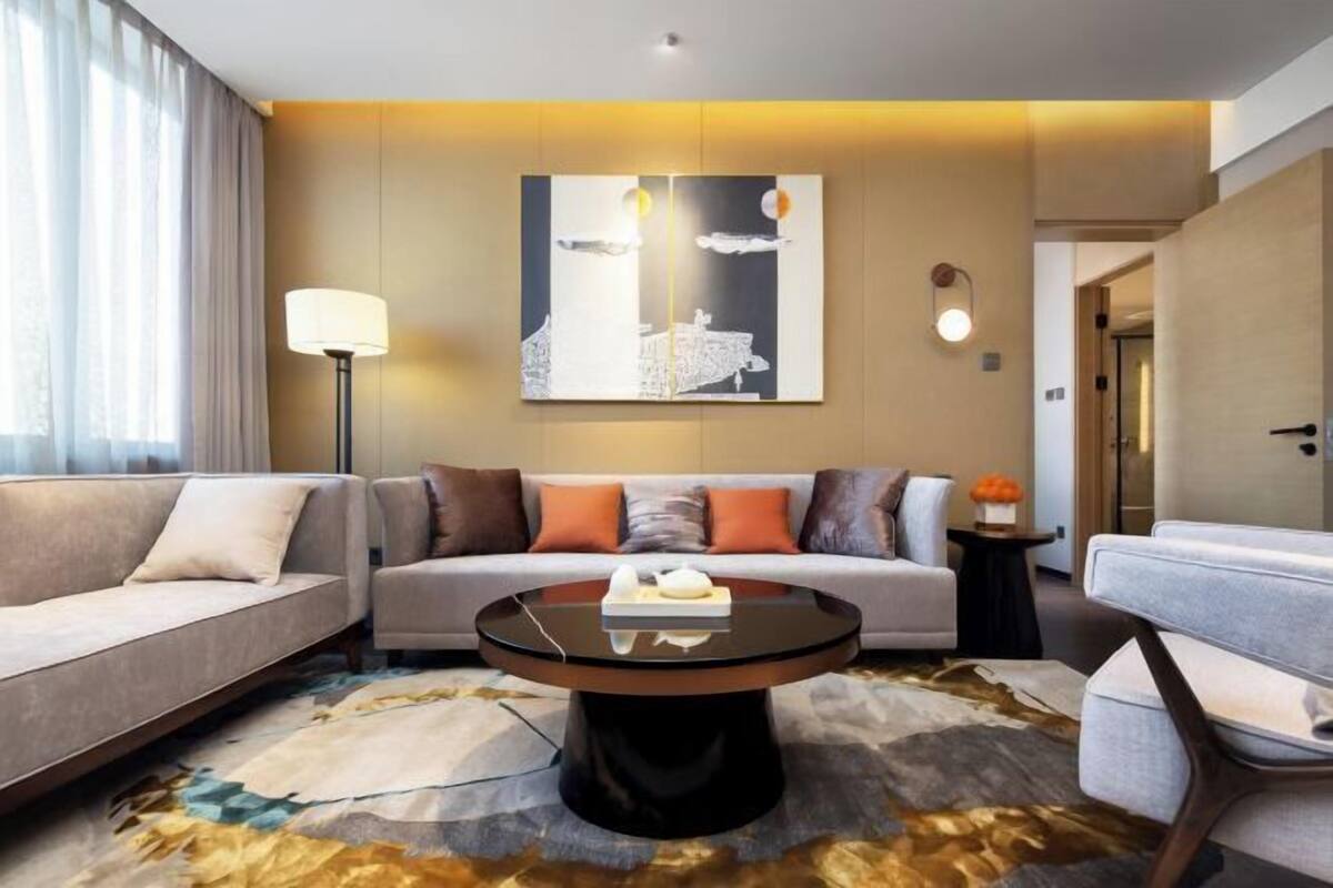 Una habitación de hotel moderna con sofá, sillón, una mesita redonda y un cuadro en la pared.